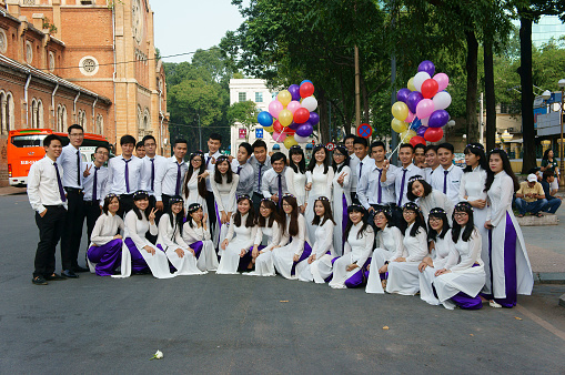 Ho Chi Minh city, Viet Nam - November 24, 2015: Crowd of Vietnamese student in traditional dress, ao dai, shooting for yearbook at Saigon Notre Dame Cathedral, Vietnam, Nov 24, 2015
