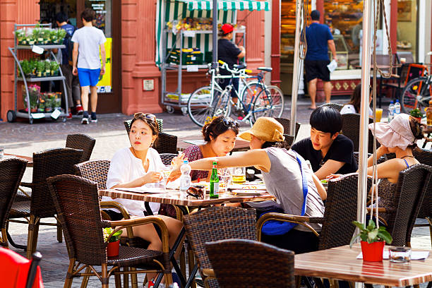 Heidelberg, Germany - July 22, 2015: Summertime shot of eating asian tourists sitting outside of restaurant at square Markt in Heidelberg. In background are more people.