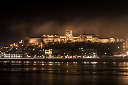 View from the Danube River of the Royal Palace in Budapest at night with the fog enveloping the structure