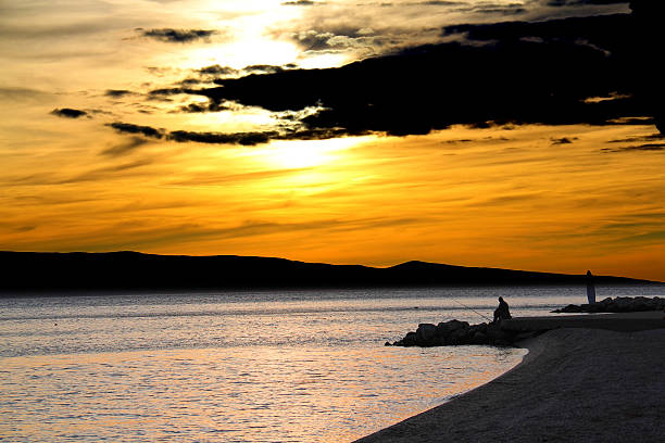 lonely fisherman in the sunset lonely fisherman at sunset, Brela, Dalmatia, Croatia malerisch stock pictures, royalty-free photos & images