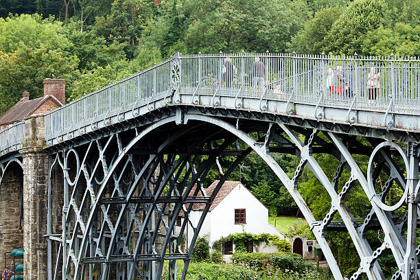 People Walking on Iron Bridge in Shropshire, England Shropshire, England - August 13, 2015: A colour photograph of people walking on the famous Ironbridge in Shropshie, under the bridge we can see a house and some trees as well as the toll house above the bridge. The site of the bridge was chosen for its high approaches on each side and the relative solid ground. ironbridge shropshire stock pictures, royalty-free photos & images