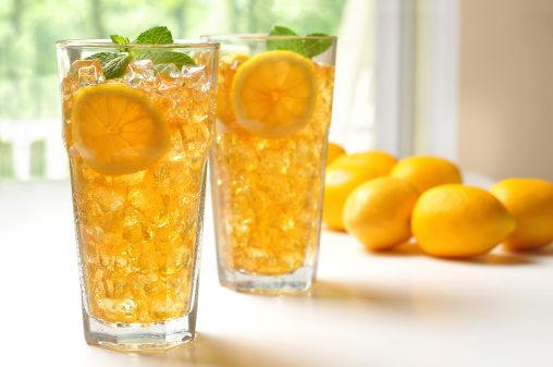 Horizontal image of two glasses of cold iced tea with lemon and mint. The glasses are sitting on the shaded porch on a summer afternoon. There is condensation on the glasses.