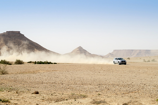 Four wheel drive car in the desert, driving fast and creating a cloud of dust. Mountains in the backgrond.