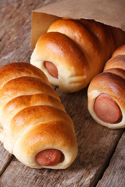 Three roll with sausage close up in a paper bag on a wooden background vertical