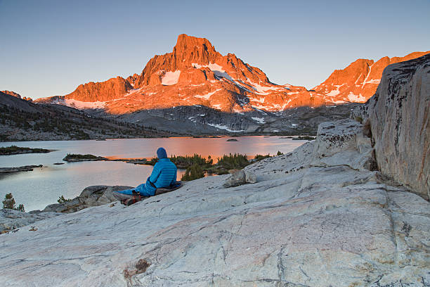 Banner Peak Sunrise Horizontal A lone backpacker with a blue stocking cap sits on a slab of granite rock and watches the early sun beams of the morning light hit Banner Peak behind Thousand Island Lake in the Ansel Adams Wilderness. pacific crest trail stock pictures, royalty-free photos & images