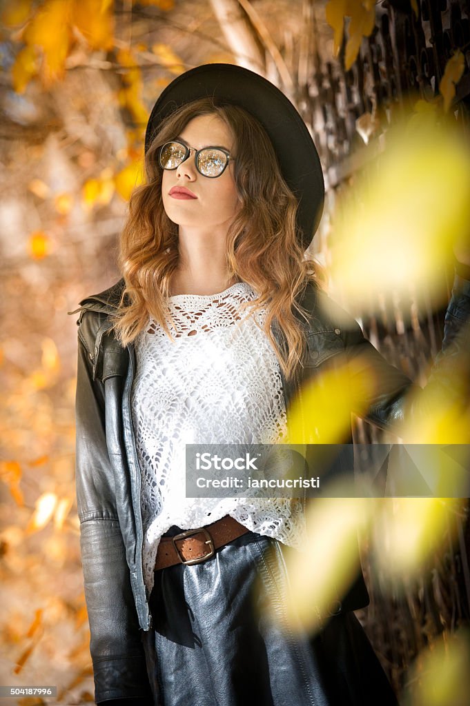 Elegant college student with glasses, hat and skirt in fall Attractive young woman in an autumnal shot outdoors. Beautiful fashionable school girl posing in park with faded leaves around. Elegant college student with glasses, hat and skirt in fall scenery . Beauty Stock Photo