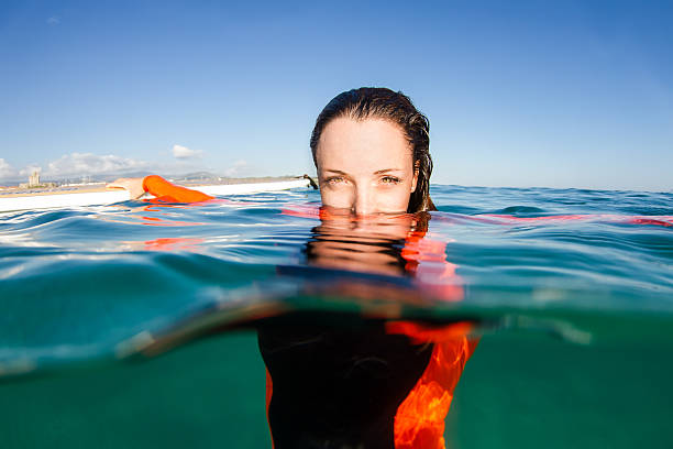 half face of woman in the water half face of woman in the water, woman swimming in the water looking to the camera and holding surfboard immersed in their work stock pictures, royalty-free photos & images