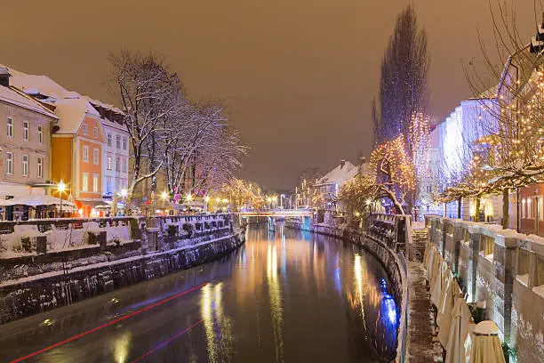 Ljubljanica river with snowy banks and streets, illuminated by christmas lights.