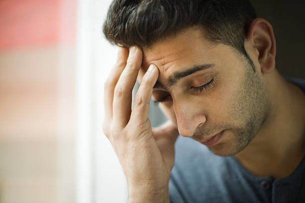 Young man holding his head out of headache near window. stock photo
