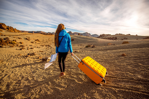 Young female traveler walking with yellow suitcase on the rocky desert in teide park on Tenerife island
