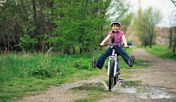 menina andar de bicicleta através de uma poça. - helmet bicycle little girls child imagens e fotografias de stock