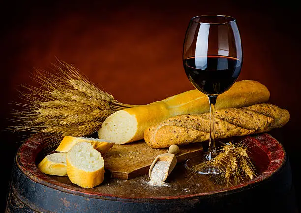 One glass of red wine and two baguettes and wheat on rustic background