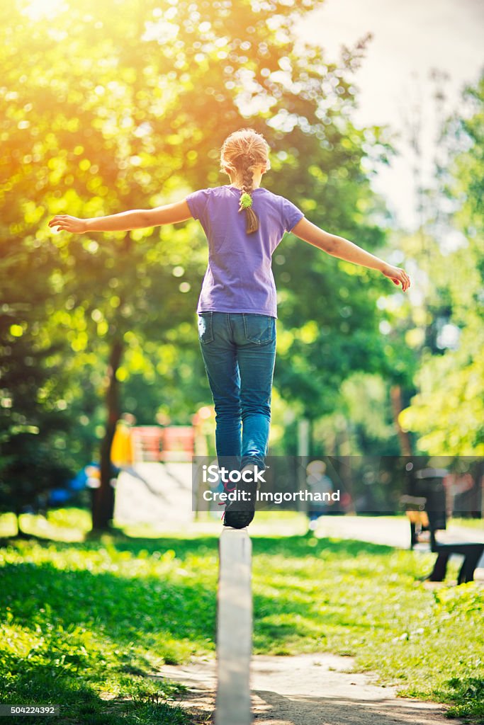 Little girl balancing on a balance beam in sunny park Little girl aged 9 holding arms outstreched  walking on a balance bean in a park. Sunny summer day. Balance Beam Stock Photo