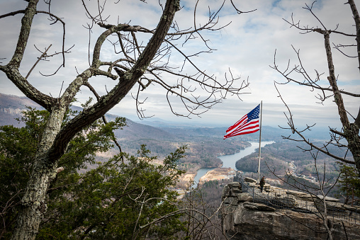 Chimney Rock, North Carolina, USA - December 7, 2012: Two visitors stand beneath an American flag on Chimney Rock in Chimney Rock State Park, North Carolina. Lake Lure is below.
