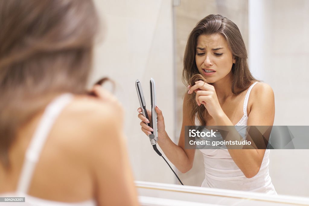 Woman straightening hair in bathroom Women Stock Photo
