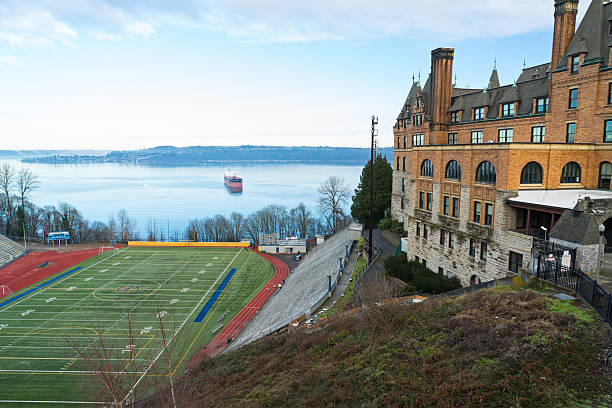 Tacoma, USA - January 9, 2016: A football field with bleachers is perched on a hill above the water.  A ship is in the background.