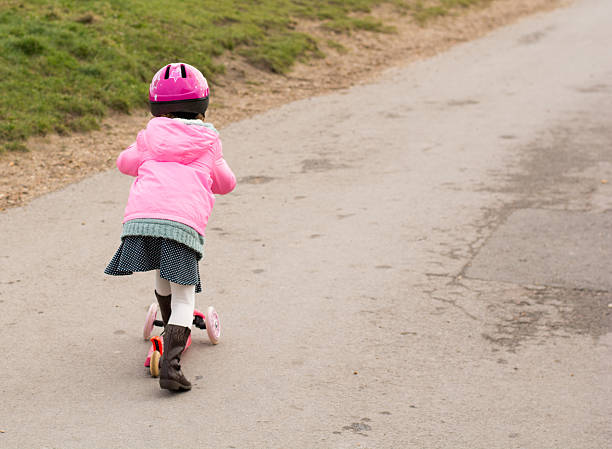 istock Young girl riding microscooter with pink helment on 504244822