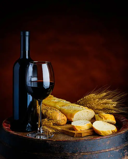 Glass and bottle of red wine, baguettes and wheat in a rustical setup