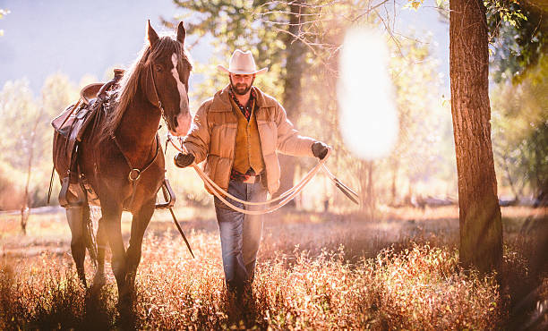 Man walks through field surrounded by trees while guiding horse