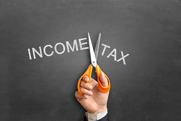 Close-up of a businessman hand using scissor cutting the word on blackboard "Income Tax become Income".