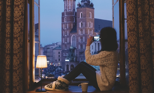 Girl sitting at the window sill and photographing with smartphone the Maricki church