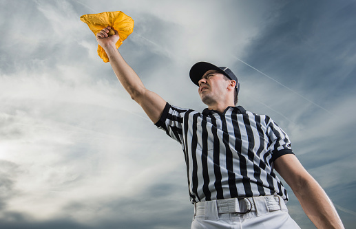 Low angle view of football judge holding a yellow flag against the sky.