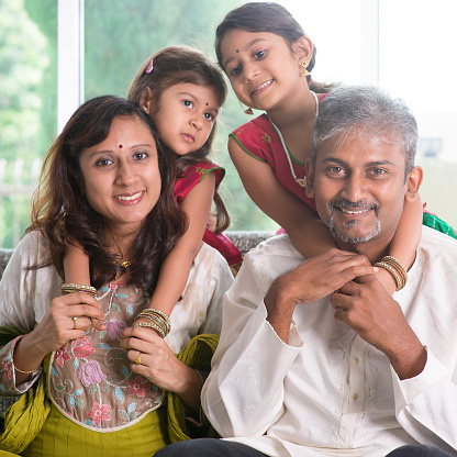 Happy Indian family at home. Asian parents piggyback their children. Adults and kids indoor lifestyle.