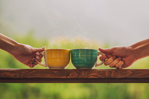 Hands holding mug with hot beverage, with tea on a wooden stand outdoors in the countryside