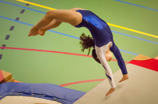 Young gymnast girl performing jump back handspring while practicing for the competition