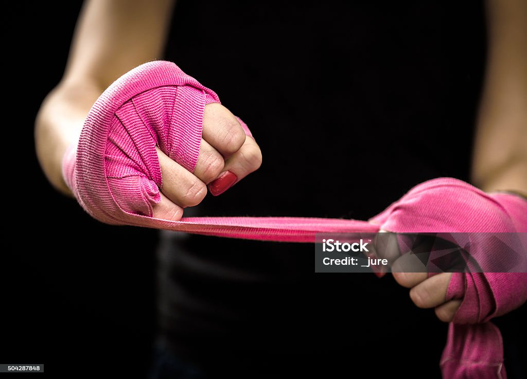 Woman is wrapping hands with pink boxing wraps Woman is wrapping hands with pink boxing wraps. Isolated on black with red nails. Strong hand and fist, ready for fight and active exercise Women Stock Photo