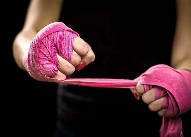 Woman is wrapping hands with pink boxing wraps. Isolated on black with red nails. Strong hand and fist, ready for fight and active exercise