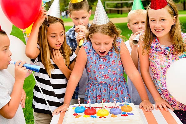 Little girl blowing out candles on her cake at her birthday party.  Her friends are next to her. 