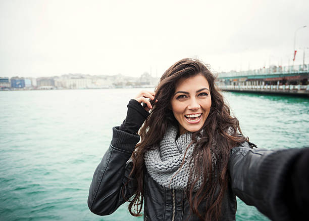 Cute Turkish Girl With Bright Smile Selfie Lovely young girl with long curly dark hair is smiling brightly and looking at camera, as if making a selfie. The image is made with a wide angle lens. Bosphorus waters, a panoramic Istanbul city view and a bridge are in the background. Image contains plenty of copy space. golden horn istanbul photos stock pictures, royalty-free photos & images