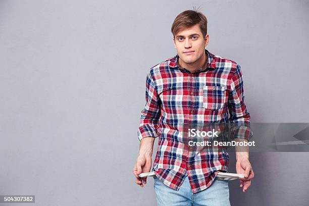 Poor Handsome Young Man In Checkered Shirt Showing Empty Pockets Stock Photo - Download Image Now