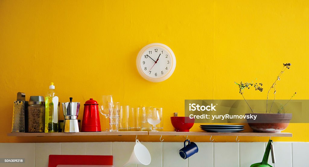 Yellow wall clock in the kitchen Yellow wall with utensils on a shelf and wall clocks Kitchen Stock Photo