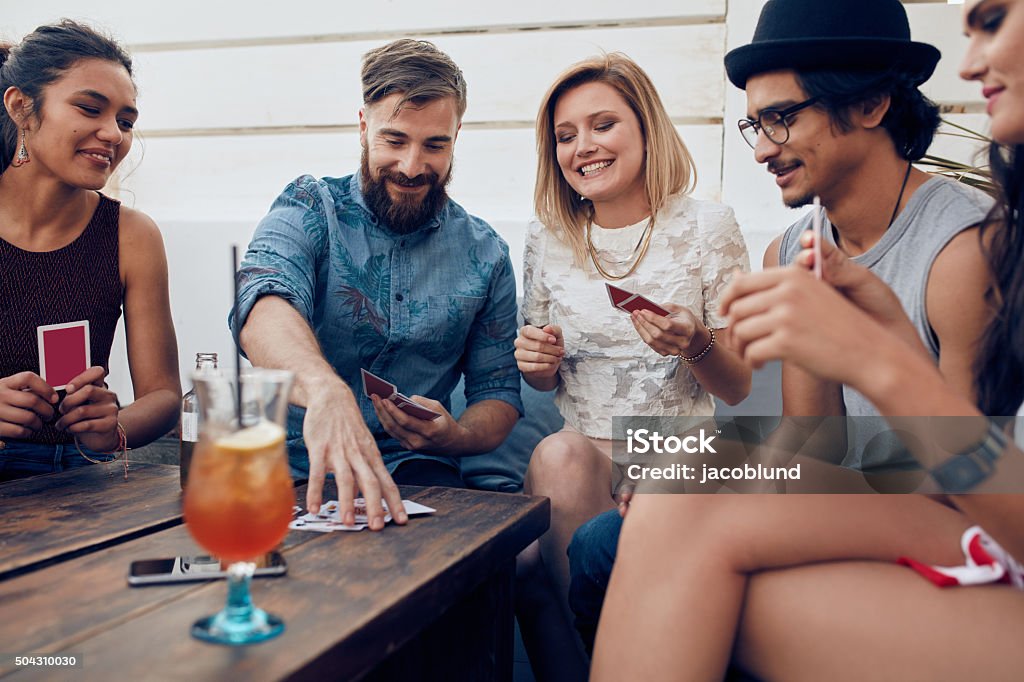 Group of friends in a party playing cards Group of friends relaxing and playing cards together. Young people hanging out together around a table during a party playing a game of cards. Playing Card Stock Photo