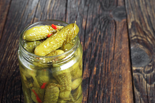 Glass jar with pickled cucumbers on a wooden table