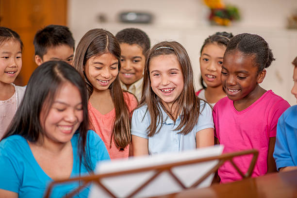 Singing Songs Together in Church A multi-ethnic group of elementary age children are standing around a piano and are singing together happily. school choir stock pictures, royalty-free photos & images
