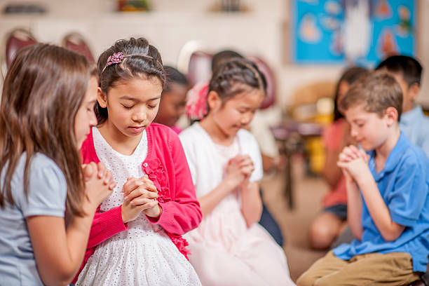Praying in Small Groups A multi-ethnic group of elementary age children are kneeling on the floor and are praying together. bible study group of people small group of people stock pictures, royalty-free photos & images