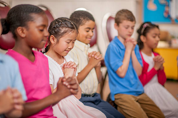 Children Praying Together A multi-ethnic group of elementary age children are kneeling on the floor and are praying together. Bible stock pictures, royalty-free photos & images