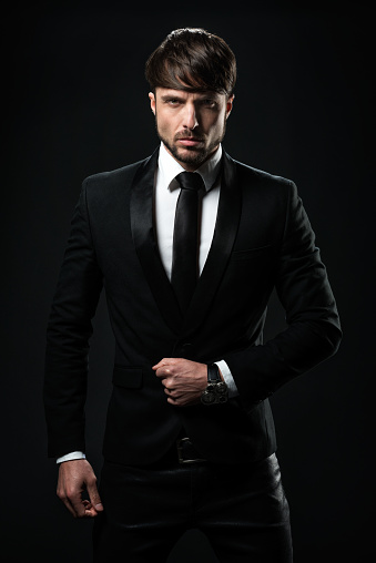 Studio portrait of a young man dressed in black tuxedo. Image on black background.