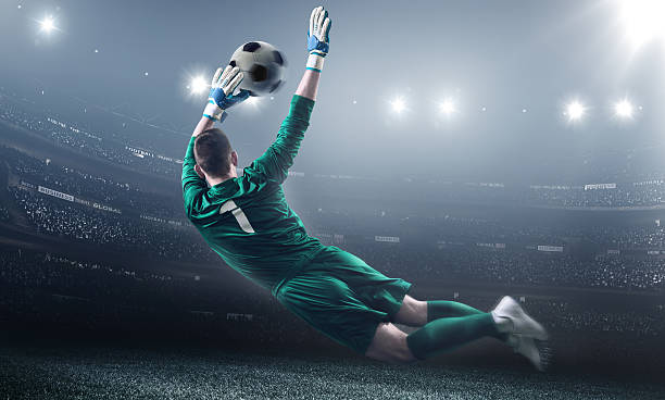 Soccer Goalkeeper in a jump Soccer goalie jumping in motion for a ball while defending his gates. The stadium is blurred behind him. Only the lights of the stadium shine brightly, creating a halo effect around the bulbs. A player is wearing unbranded soccer uniform. storm cloud sky dramatic sky cloud stock pictures, royalty-free photos & images