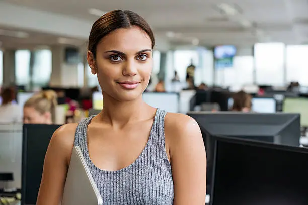 Portrait of ethnic aboriginal Australian businesswoman in a  office holding a laptop computer. Young female business professional at modern workplace in Australia. 