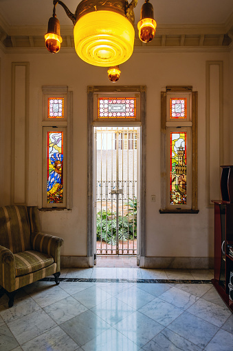 Interior of old Havana villa. Suburbs of Vedado, Havana. View of the back yard patio thru iron bars on the door. Old rustic stained glass windows on the wall of the study.