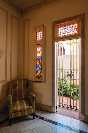 Interior of old Havana villa. Suburbs of Vedado, Havana. View of the back yard patio thru iron bars on the door. Old rustic stained glass windows on the wall of the study.