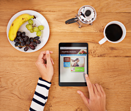 Shot of a woman using a digital tablet at the breakfast table- ALL screen content on this image is created from scratch by Yuri Arcurs'  team of professionals for this particular photo shoot