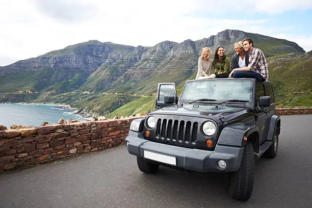 Shot of a group of friends relaxing on the roof of their truck with a mountainous background
