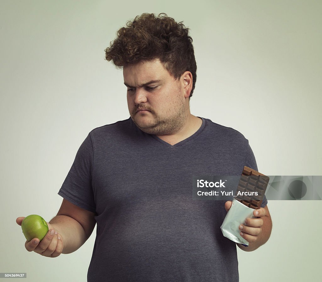 Sorry mr apple - you lose this round Cropped shot of an overweight man deciding between an apple and a chocolate bar Contemplation Stock Photo
