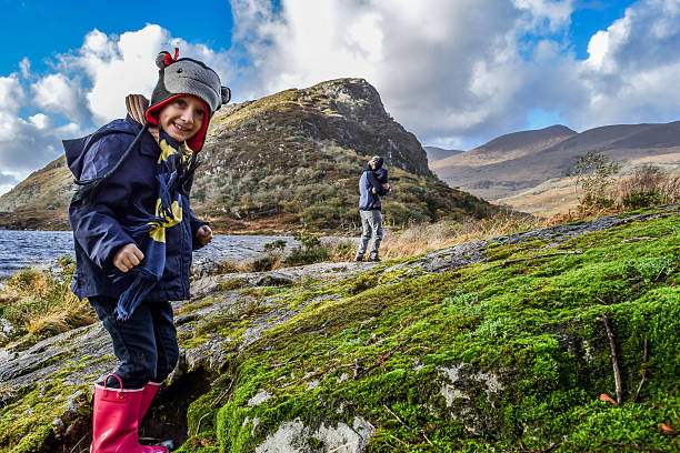 Exploring Little girl smiles at the camera, her father and sister inthe background, whie exploring a wilderness area in scenic Ireland killarney lake stock pictures, royalty-free photos & images