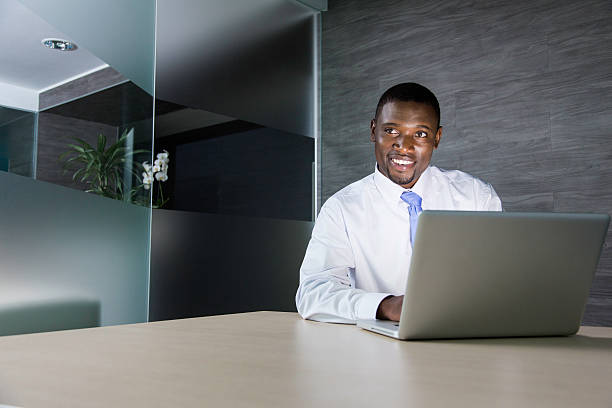 African businessman typing on his laptop with a smile. Cape Town, South Africa.